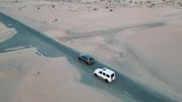 一架无人驾驶飞机驾驶着两辆昂贵的汽车在空旷的路上在沙漠的沙滩上飞行 空中景观 慢动作 — 图库视频影像