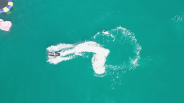 Dubai, BAE - 320 2023: Bir İHA arka planda Dubai yatı olan bir yatın yanında, denizde jet ski kullanan insanların üzerinde uçuyor. Hava görüntüsü, yavaş çekim