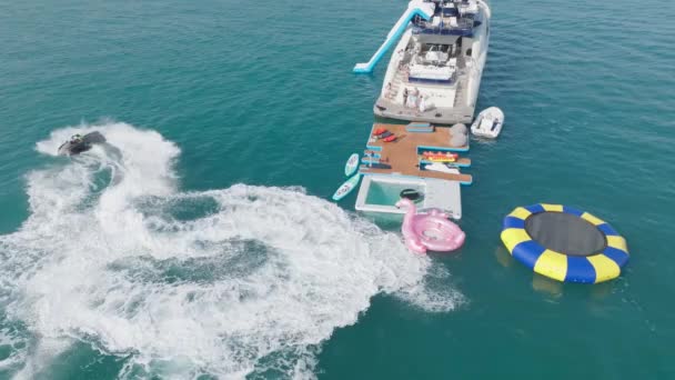 アラブ首長国連邦 ドバイ 2023 ヨットの隣の海でジェットスキーに乗っている人々をドローンが飛ぶ エアリアルビュー スローモーション — ストック動画