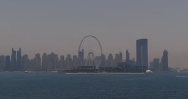 İnsansız hava aracı denizin dalgaları üzerinden kıyıdaki şehre doğru uçuyor. Dubai, Birleşik Arap Emirlikleri. Hava görünümü