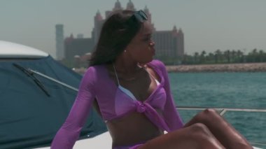 Özel bir teknenin güvertesinde, genç esmer bir kadının yanında meyve salatası. Beyaz bikinili ve şeffaf pelerinli bir kadın teknenin pruvasında oturuyor ve meyve yiyor. Yavaş çekim.