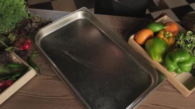 Eldivenli şef, sebze ve otların arasında bir masada duran bir tepsiye balık atıyor. Yavaş Hareket, Kapat.