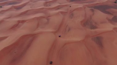 Bir dron, Birleşik Arap Emirlikleri 'nde çölün kum tepelerinden geçen dört tekerlekli bisikletlerin üzerinden uçuyor. Hava görünümü