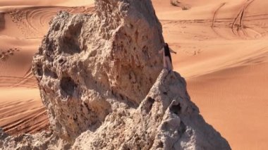 Bir dron, Birleşik Arap Emirlikleri 'nin kumlu çölündeki bir uçurumda dua eden şaman kılığında sakallı bir adamın etrafında uçuyor. Hava görünümü