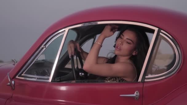長い黒髪と赤いヴィンテージカーの中に座っている明るいメイクを持つ若い壮観な女性 スローモーション — ストック動画