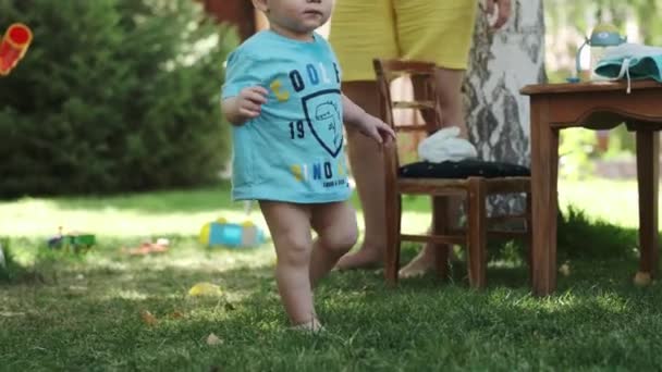 Tシャツの小さな男の子とズボンなしの男の子は 芝生の上で裸足を歩いています 母親は彼と遊んでいる スローモーション 晴れた日 — ストック動画