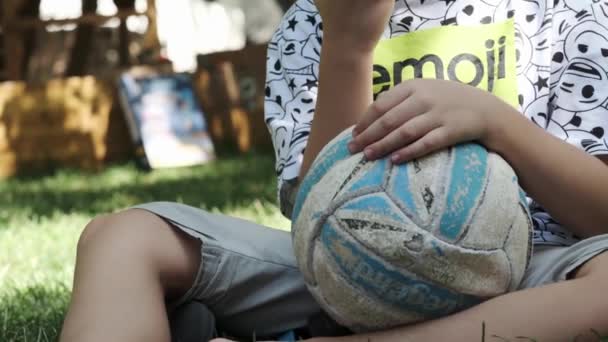 Nastolatek Szortach Koszulce Boso Siedzi Trawie Parku Piłką Pod Pachą — Wideo stockowe