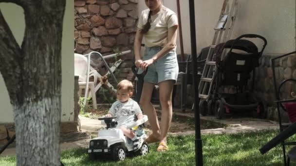 Młoda Matka Krótkich Spodenkach Jeździ Swoim Synkiem Zabawkowym Samochodzie Park — Wideo stockowe