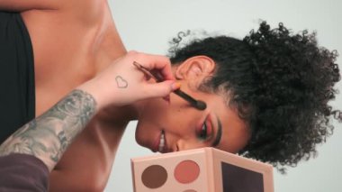 Dubai, BAE - 710 2023: Profesyonel makyaj ustası kıvırcık saçlı genç bir modele boya uyguluyor. Dikey, Yavaş Hareket, Kapat.