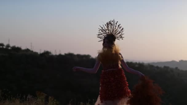 スパイシーツで作られたヘッドドレスの若い女性と 秋の花のドレスには 山の夕日を背景に葉が手元にある乾燥した枝があります スローモーション — ストック動画