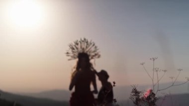 Sonbahar tasarımcı elbisesi içinde genç bir kadın mankenle film ekibi ve dağlarda gün batımının arka planında dikenlerden yapılmış bir başlık. Yavaş Hareket.