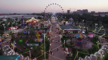 Taşkent, Özbekistan - 84 2022: Bir insansız hava aracı lunaparkta atlıkarıncalı ve dönme dolaplı uçuyor. Gece, hava manzaralı.