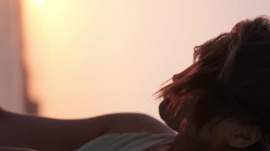 Parlak makyajlı, kırmızı elbiseli genç bir kadının dikey portresi çölün ortasında denizin üzerinde gün batımının arka planına karşı. Yavaş Hareket, Kapat