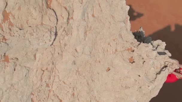 ドローンは 砂漠の砂の真ん中に崖の上に立っている赤いドレスの若い女性の周りを飛び回ります エアリアルビュー — ストック動画