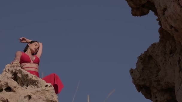 Młoda Kobieta Czerwonej Sukience Siedzi Skale Środku Pustyni Przeciwko Błękitnemu — Wideo stockowe