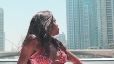 Dubai gökdelenlerinin arka planına karşı özel bir teknenin güvertesinde kısa parlak elbiseli esmer bir kadın. BAE, Ağır çekim