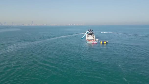 アラブ首長国連邦 ドバイ 2023 ドローンは バックグラウンドでドバイとヨットの隣に海上でジェットスキーに乗っている人々を飛ぶ エアリアルビュー スローモーション — ストック動画