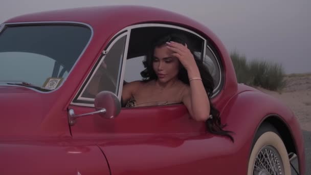 長い黒髪と赤いヴィンテージカーの中に座っている明るいメイクを持つ若い壮観な女性 スローモーション — ストック動画