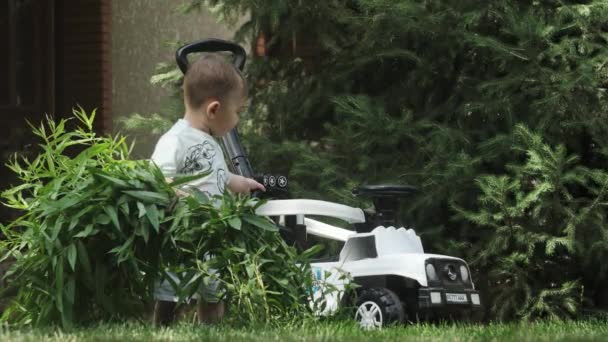 一个穿着T恤和短裤的小男孩开着他的玩具车在一个开花的花园里玩耍 慢动作 — 图库视频影像