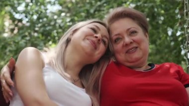 Evinin yanındaki bahçede salıncakta sallanan küçük bir kızı olan yetişkin bir anne. Sarılmak, konuşmak ve gülmek. Yavaş Hareket, Kapat.