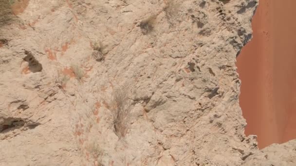 ドローンは 砂漠の砂の真ん中に崖の上に立っている赤いドレスの若い女性の周りを飛び回ります エアリアルビュー — ストック動画
