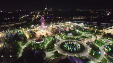 Bir dron lunaparkın üzerinde atlı karınca ve dönme dolap ile uçuyor. Gece, hava manzaralı.