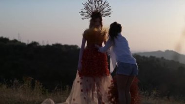 Sonbahar tasarımcı elbisesi içinde genç bir kadın mankenle film ekibi ve dağlarda gün batımının arka planında dikenlerden yapılmış bir başlık. Yavaş Hareket.