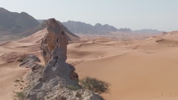 在阿拉伯联合酋长国的沙滩上 一架无人驾驶飞机在一个留着胡子的男人周围飞来飞去 他打扮成一个萨满 在悬崖上祈祷 空中景观 — 图库视频影像