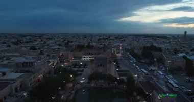 Eski Buhara, Özbekistan 'daki evlerle çevrili antik bir Lyab-i Hauz kompleksinin üzerinde bir İHA uçuyor. Bulutlu bir gece. Hava Görünümü.