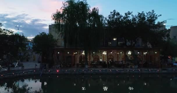 ドローンは 夜に古代の複雑なウルグベック マドラの近くのプール水の表面を飛ぶ オールド ブハラ ウズベキスタン エアリアルビュー — ストック動画