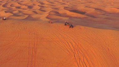 Bir dron, Birleşik Arap Emirlikleri 'nde çölün kum tepelerinden geçen dört tekerlekli bisikletlerin üzerinden uçuyor. Hava görünümü