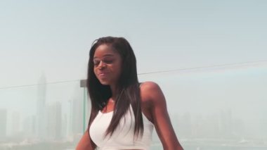 Dubai, BAE 'ye tepeden bakan cam bir balkonda beyaz takım elbiseli esmer bir kadın. Yavaş Hareket.