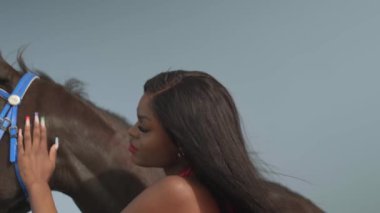 Kırmızı elbiseli genç esmer bir kadın okyanus kıyısında bir atın yanında duruyor. Yavaş çekim.