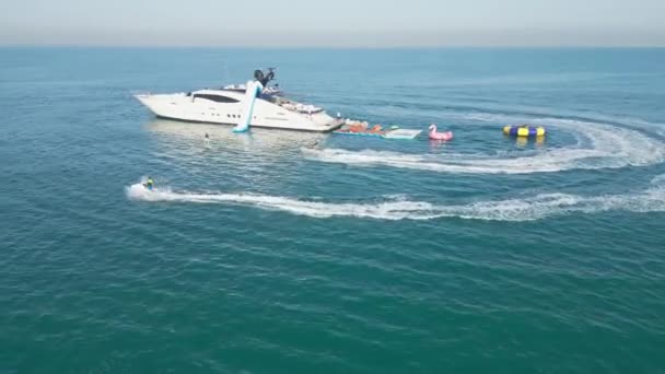 アラブ首長国連邦 ドバイ 2023 ドローンは 背後にあるドバイとヨットの周りの海上にジェットスキーに乗っている人々と電気ホイルボードを飛ぶ エアリアルビュー スローモーション — ストック動画