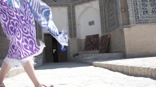 一位身穿东方长袍头戴便帽的年轻女子穿过一座古老的东方城市 乌兹别克斯坦慢动作 — 图库视频影像