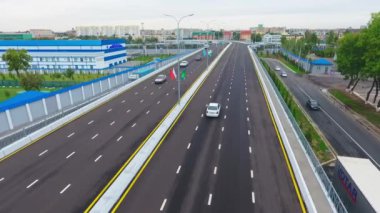 İnsansız hava aracı hareket halindeki arabalarla şehrin yollarında ve otoyollarında uçuyor. Bulutlu bir yaz günü. Hava Görünümü.