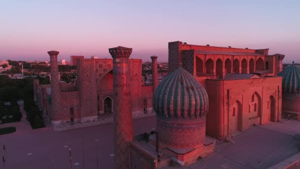 ウズベキスタンのサマルカンドにある複雑なビビ カニム モスクの近くでドローンが飛ぶ 建物はピンクの夜明けの光で照らされています 雲のない朝 エアリアルビュー — ストック動画