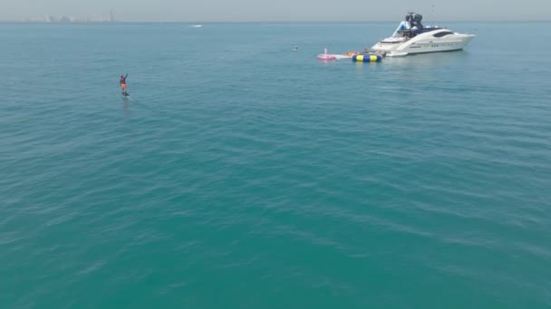 一架无人驾驶飞机在一艘私人游艇旁边的公海上 飞越了一个坐着电翼板航行的人 空中景观 慢动作 — 图库视频影像