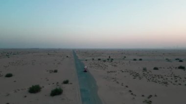 Bir İHA çölün kumları arasında boş bir yolda giden iki pahalı arabanın yanından uçuyor. Hava Görünümü, Yavaş Hareket.