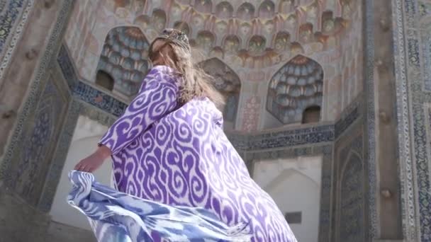 一位身穿东方长袍头戴便帽的年轻女子穿过一座古老的东方城市 乌兹别克斯坦慢动作 — 图库视频影像
