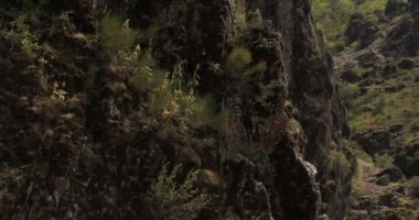 Bir dron, dik bir yamaçta tek kolunda asılı duran genç bir atletik kadın dağcının etrafında uçuyor. Hava Görünümü