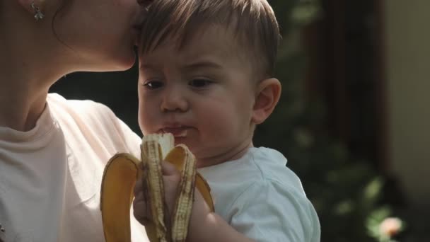 Filho Pequeno Nos Braços Uma Jovem Mãe Come Uma Banana — Vídeo de Stock