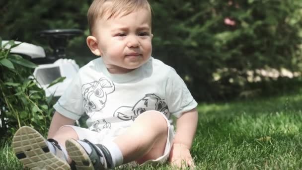 小さな男の子が公園の草の上に座り プラスチック製のボールで遊んでいる スローモーション — ストック動画