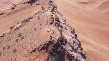 Çölün kum tepeleri arasında ıssız bir kayanın üzerinden bir dron uçuyor. Hava görünümü.