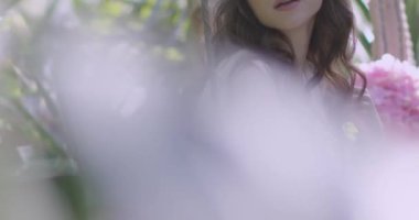 A young beautiful girl in a wreath of flowers swings on a swing among a green garden. Slow motion