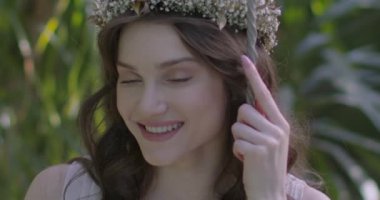 A young beautiful girl in a wreath of flowers swings on a swing among a green garden. Slow motion