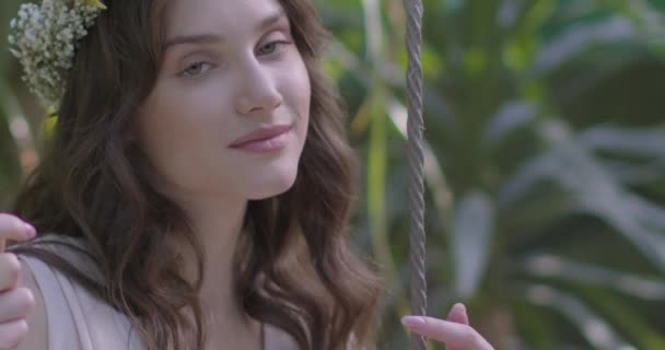 一个年轻美丽的姑娘 戴着花环 在一个绿色的花园里荡秋千 慢动作 — 图库视频影像