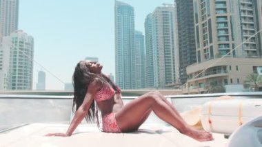Dubai gökdelenlerinin arka planına karşı özel bir teknenin güvertesinde kısa parlak elbiseli esmer bir kadın. BAE, Ağır çekim