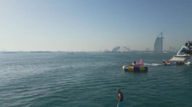 Dubai, BAE - 320 2023: İnsansız hava aracı jet ski kullanan insanların üzerinde uçuyor ve arka planında Dubai olan bir yatın etrafında elektrikli folyo var. Hava Görünümü, Yavaş Hareket.