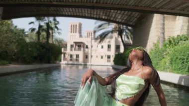 Elbiseli rahat ırklar arası bir kadın Dubai 'de bir kanaldan geçen bir teknenin pruvasında oturuyor. Güzellik, sağlık ve özgüven, yavaş çekim
